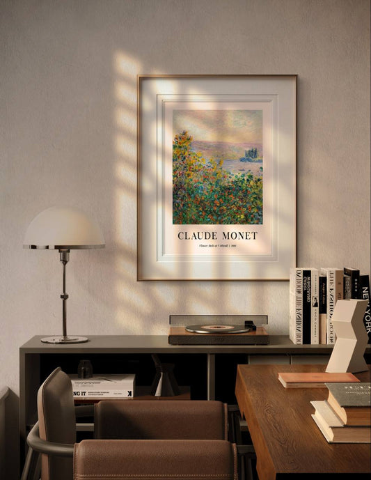 The Monet "Flower Beds at Vétheuil" poster, framed and hanging above a desk, is softly illuminated by sunlight in a cozy, modern room with books and a lamp.