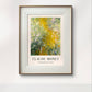 The framed "The Path through the Irises" painting by Monet, featuring a lush garden scene with green and yellow hues, is displayed against a minimalist white wall, bringing nature indoors.