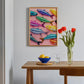 Colorful fish artwork on a wall above a wooden table with a bowl, glass, and vase of tulips.