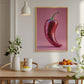 Framed artwork of a red chili pepper on a wall above a dining table with decor items.