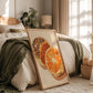 Framed artwork of dried oranges on a bed in a bedroom with natural light.