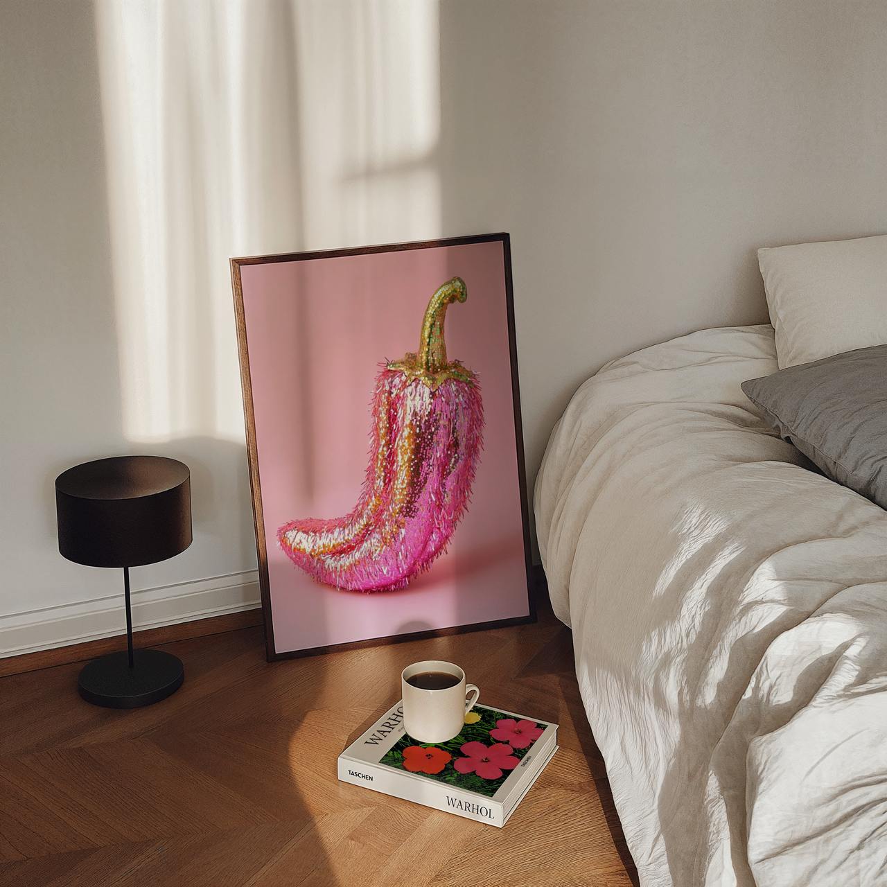 Framed artwork of a pink and gold pepper on a bedside table with a cup and book.