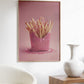 Framed artwork of pink fries on a wall above a white chair and wooden side table.