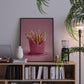 Framed artwork of pink fries on a bookshelf with decor items.
