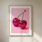 Poster featuring two bright pink glitter cherries with stems on a pastel pink background, framed in wood.
