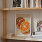 Wooden shelf with books and a framed picture of oranges