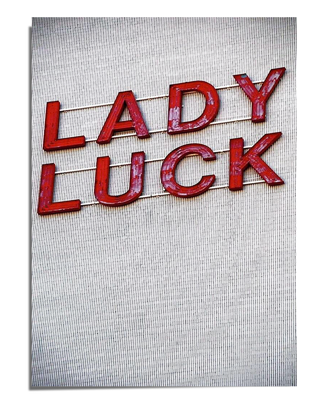 A white textured background featuring the words "Lady Luck" in three-dimensional red letters, connected by thin gold wires, creating a vintage and elegant visual effect.