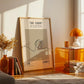 Framed artwork on a wall with a side table and decorative items in a room.