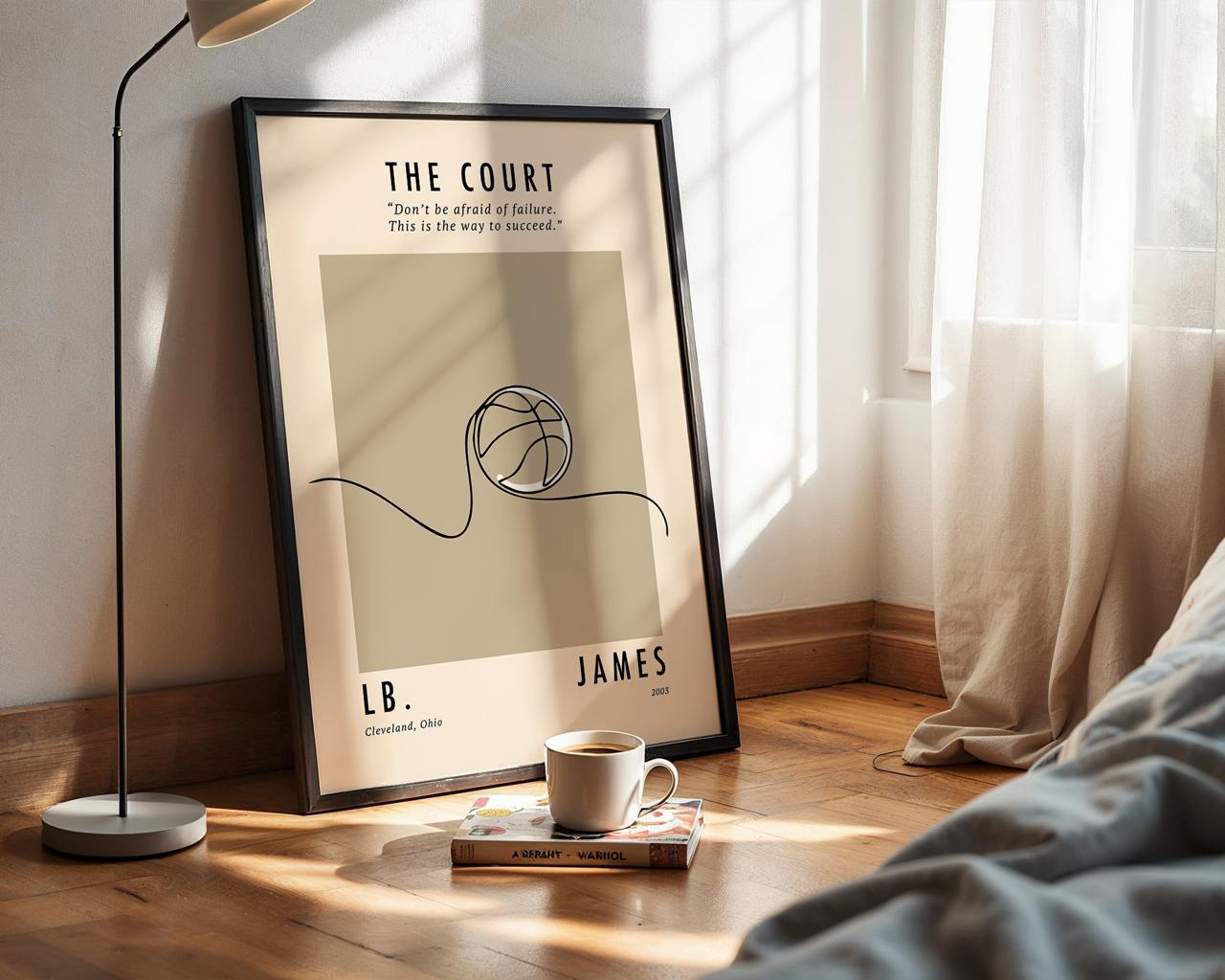 Framed poster of a basketball design on a wall next to a bed with a lamp and cup.