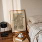 Room interior with a bed, lamp, and framed artwork on a wall.