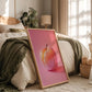 Framed artwork of a colorful apple on a bed in a bedroom.