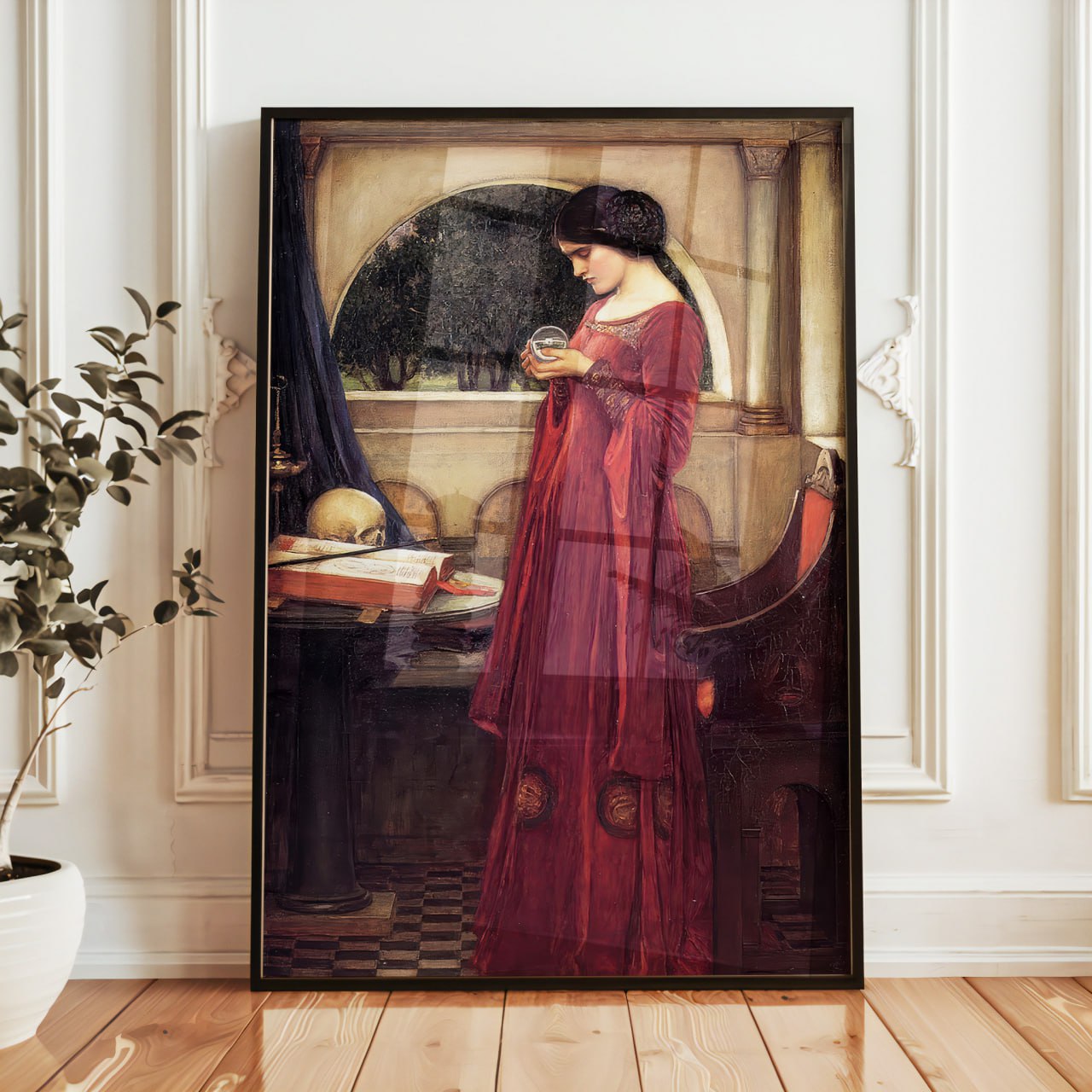 The painting shows a woman in a flowing red dress holding a crystal ball, gazing thoughtfully. Her dark hair frames her face as she stands in a dim room with a large arched window revealing greenery outside. A skull and books sit on the table, adding a sense of mystery and elegance typical of the Pre-Raphaelite style.