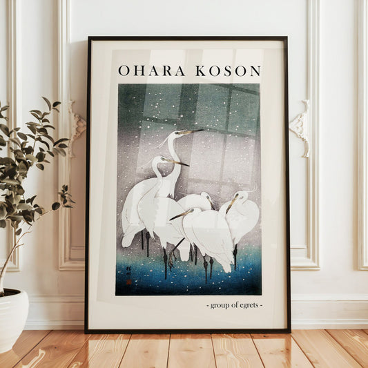 The image displays a framed print of a traditional Japanese artwork titled “Group of Egrets” by Ohara Koson, leaning casually against an elegant wall with detailed molding in a bright and sophisticated room.