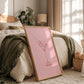 Framed pink print of a cocktail glass on a bed in a cozy bedroom.