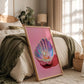 Framed artwork of a colorful shell with a pearl on a bedside table in a bedroom.