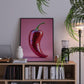 Framed artwork of a red chili pepper on a bookshelf with decorative items.