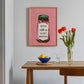 Framed artwork on a wall above a wooden table with a bowl, glass, and vase of tulips.