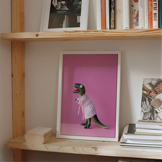 Framed picture of a dinosaur in a lab coat on a pink background, displayed on a wooden shelf with books.