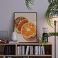 Framed artwork of oranges on a bookshelf with decorative items