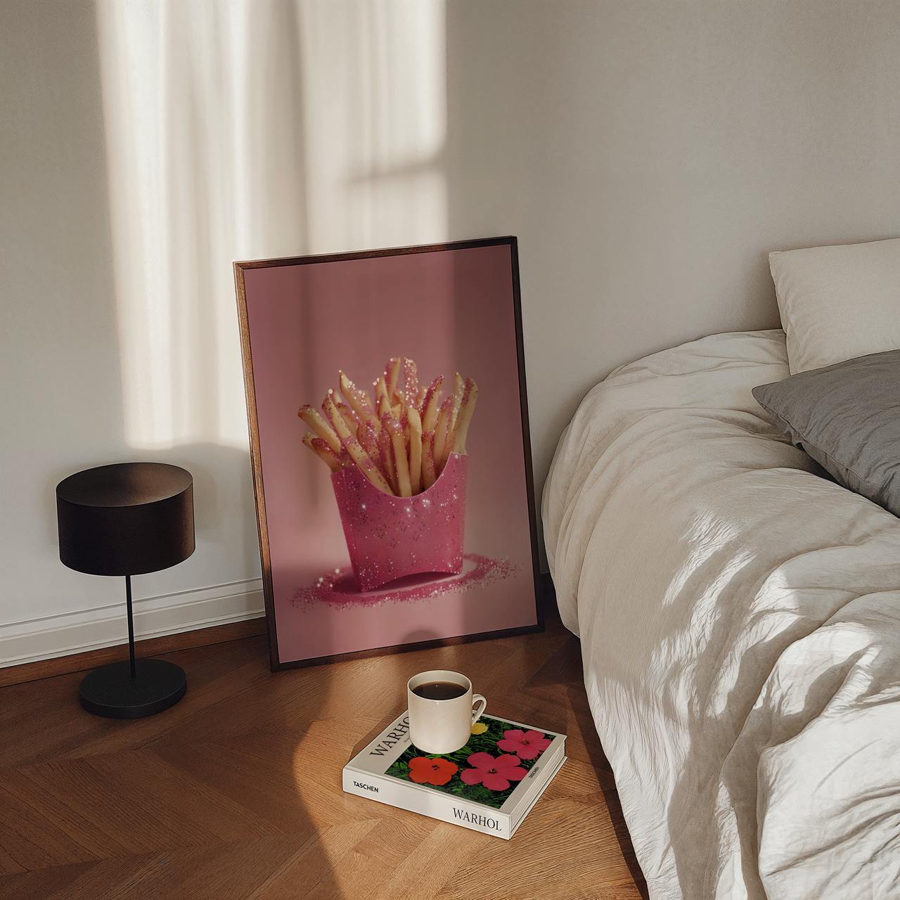 Framed picture of French fries on a bedside table next to a bed with a lamp and book.