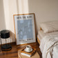 Framed poster on a wall above a bed with a lamp and coffee cup on a side table.