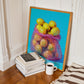Framed artwork of a colorful bag of fruit on a wall next to books and a coffee cup.