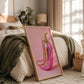 Framed artwork of a pink and gold pepper on a bed in a bedroom.